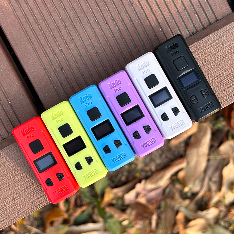 A group of different colored electronic devices including the Yocan Kodo Pro Battery on a wooden bench.