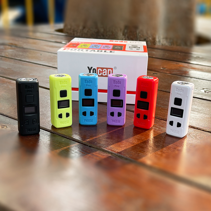 A group of different colored Yocan Kodo Pro Battery vaporizers on a wooden table.