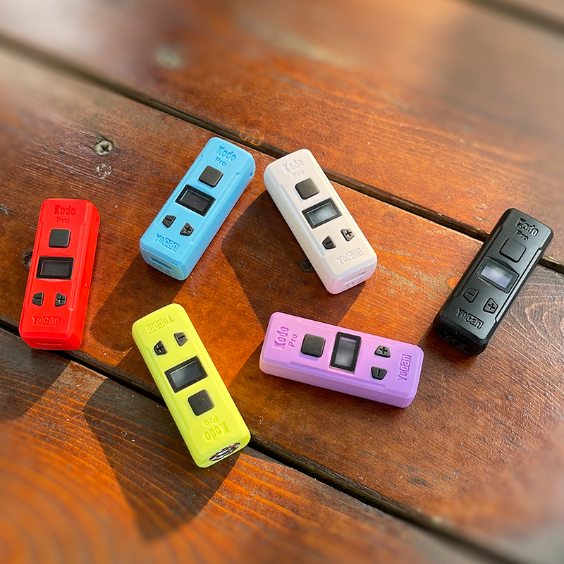 A group of electronic devices on a wooden table with the Yocan Kodo Pro Battery.
